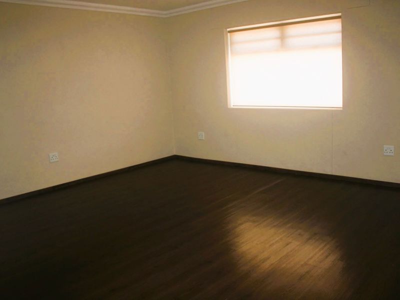 A clean, empty bedroom featuring dark laminate flooring, neutral walls, and a fitted roller blind, providing a versatile space ready for personalization.