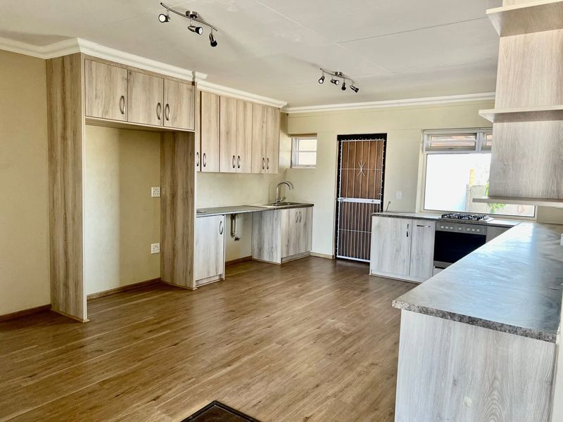 A clean, modern kitchen featuring light wood-grain cabinetry, laminate flooring, built-in oven and hob, and ample counter space in an open-plan layout.