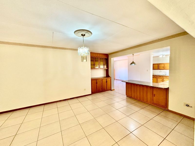 Spacious open-plan living and dining area featuring tiled flooring, built-in wooden cabinetry, and a breakfast bar connecting to the kitchen.