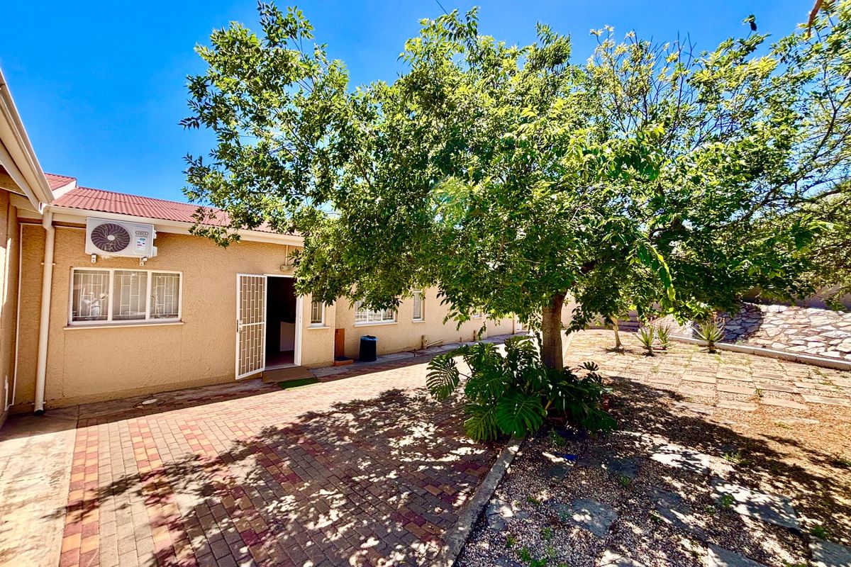 Rear exterior view featuring a paved patio area, mature tree, and wall-mounted air conditioning unit.