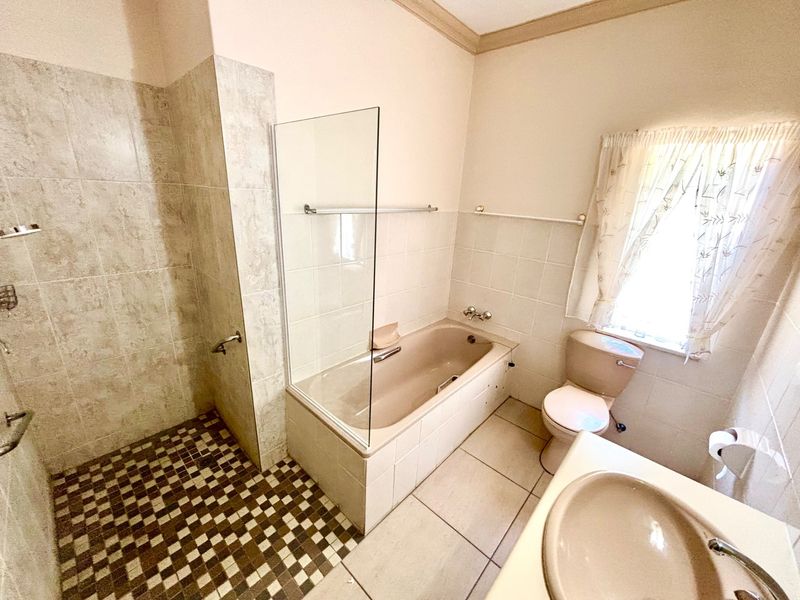 A functional bathroom featuring a built-in bathtub with a glass screen, a separate tiled shower area, a toilet, and a pedestal washbasin.