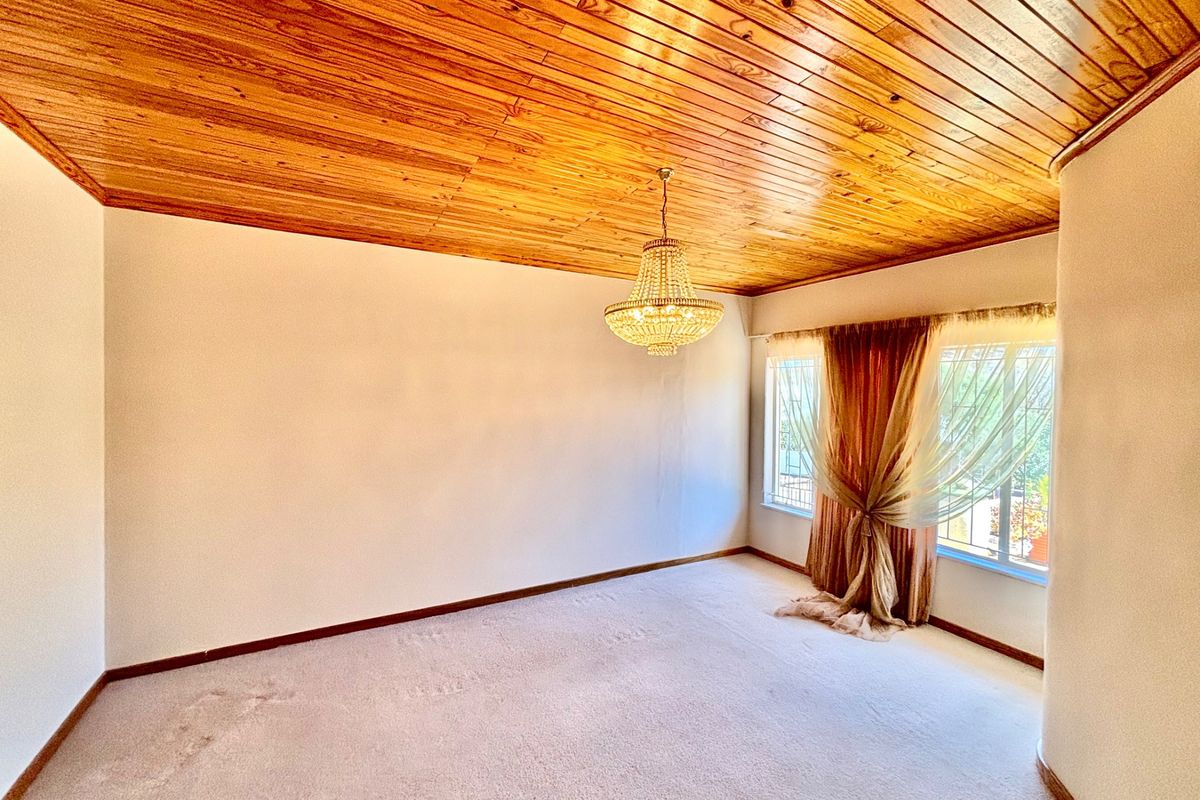 Spacious bedroom featuring a warm timber-clad ceiling, a classic crystal chandelier, and neutral carpeting, offering a blank canvas for personalization.