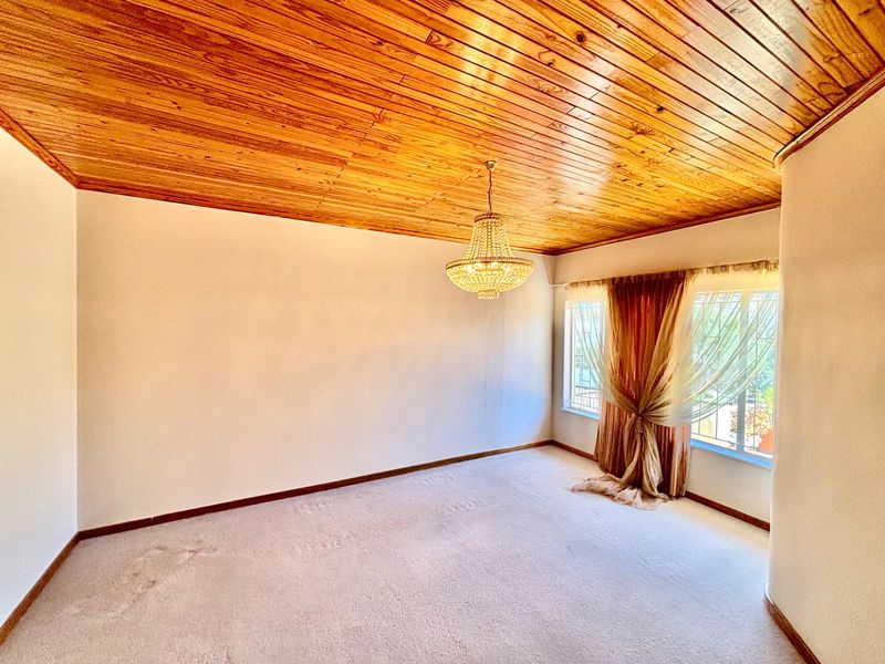 Spacious bedroom featuring a warm timber-clad ceiling, a classic crystal chandelier, and neutral carpeting, offering a blank canvas for personalization.