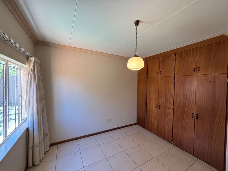 A bright, empty bedroom featuring tiled flooring, a classic pendant light, and extensive built-in wooden cabinetry for storage.