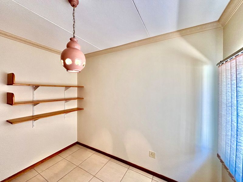 A clean, empty bedroom featuring tiled flooring, built-in wall shelving, decorative ceiling cornice, and vertical window blinds.