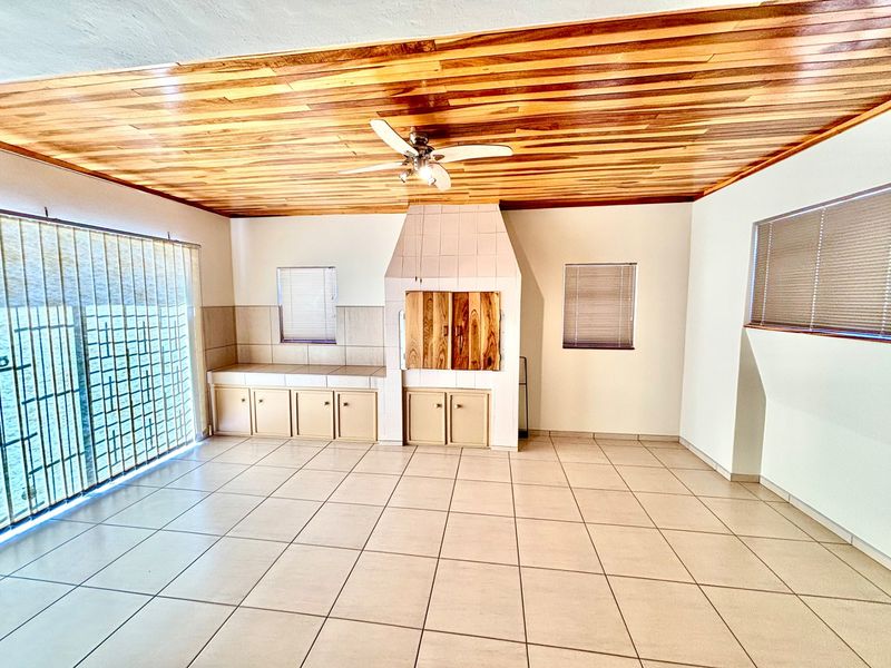 Spacious living area featuring a timber-clad ceiling, tiled flooring, and a built-in braai with integrated cabinetry.