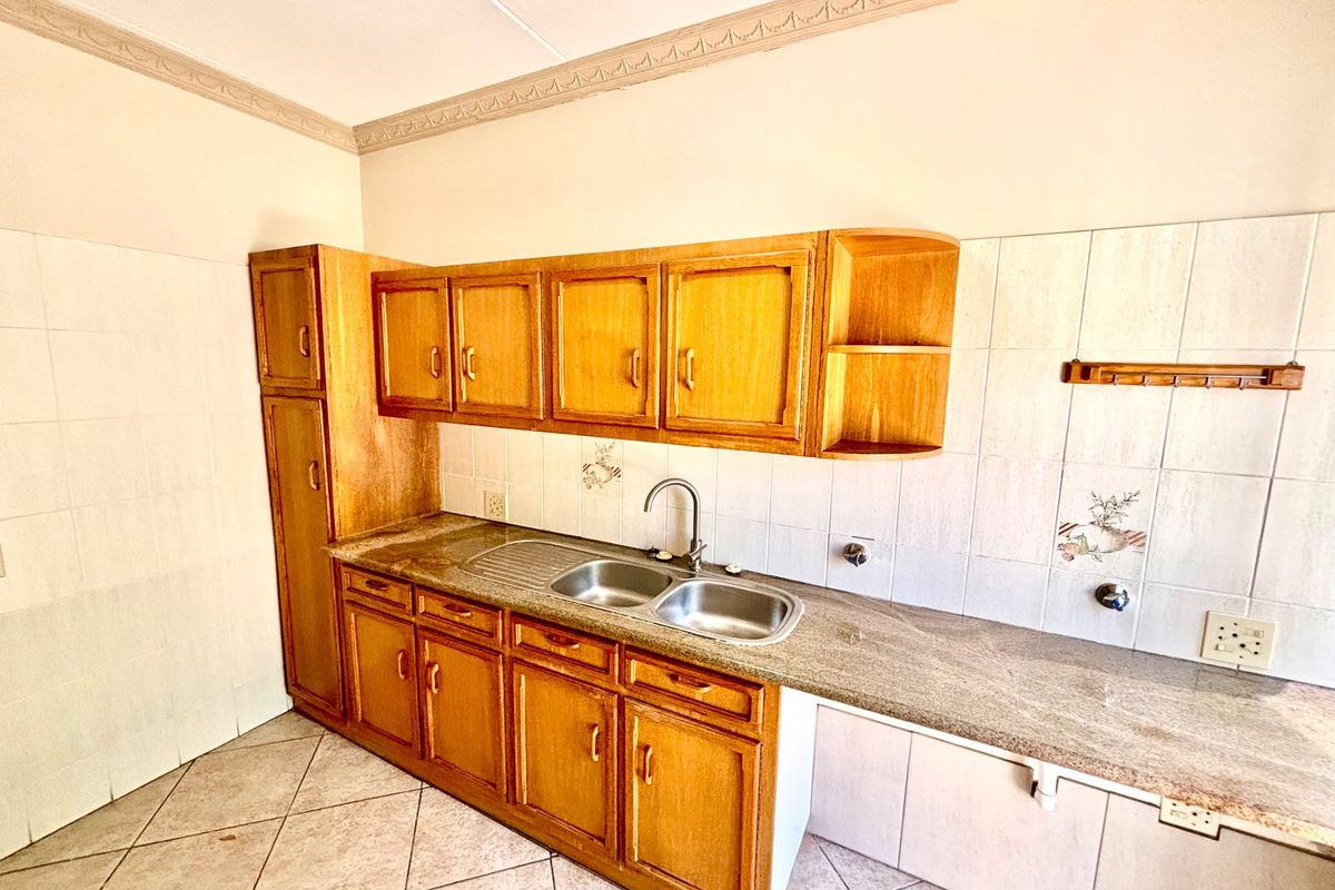 A functional kitchen featuring wooden cabinetry, granite countertops, a double stainless steel sink, and tiled splashbacks with decorative accents.