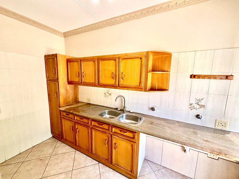 A functional kitchen featuring wooden cabinetry, granite countertops, a double stainless steel sink, and tiled splashbacks with decorative accents.