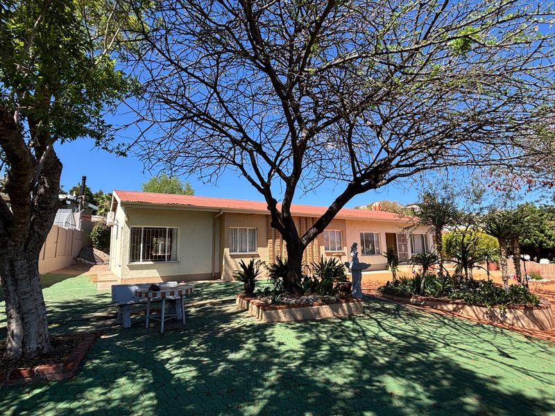 Rear view of the house featuring a paved patio area, established garden beds, and a corrugated metal roof with security bars on the windows.