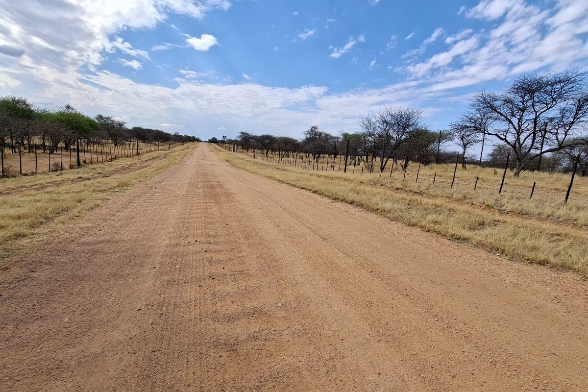 A view of a rural dirt access road flanked by wire fencing and natural vegetation on a farm property.