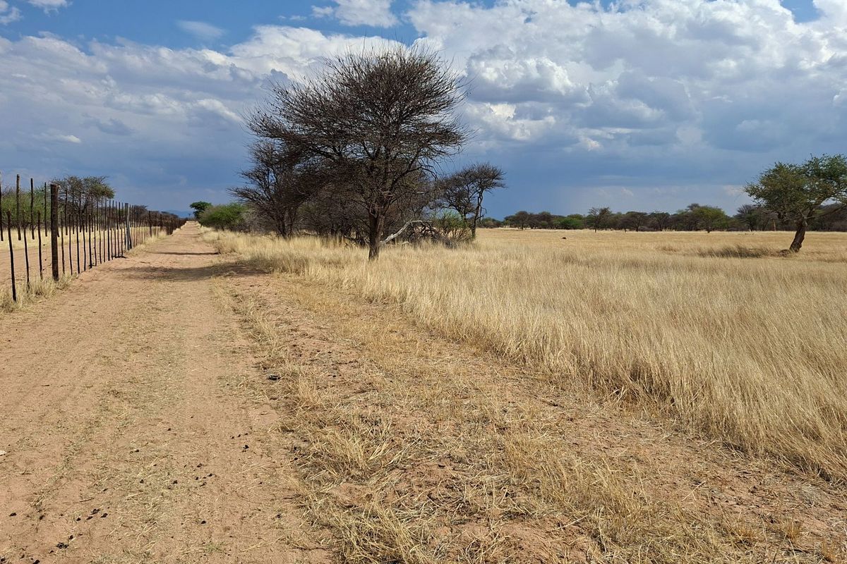A view of a rural farm property featuring a dirt track running alongside a wire fence and open grassland.
