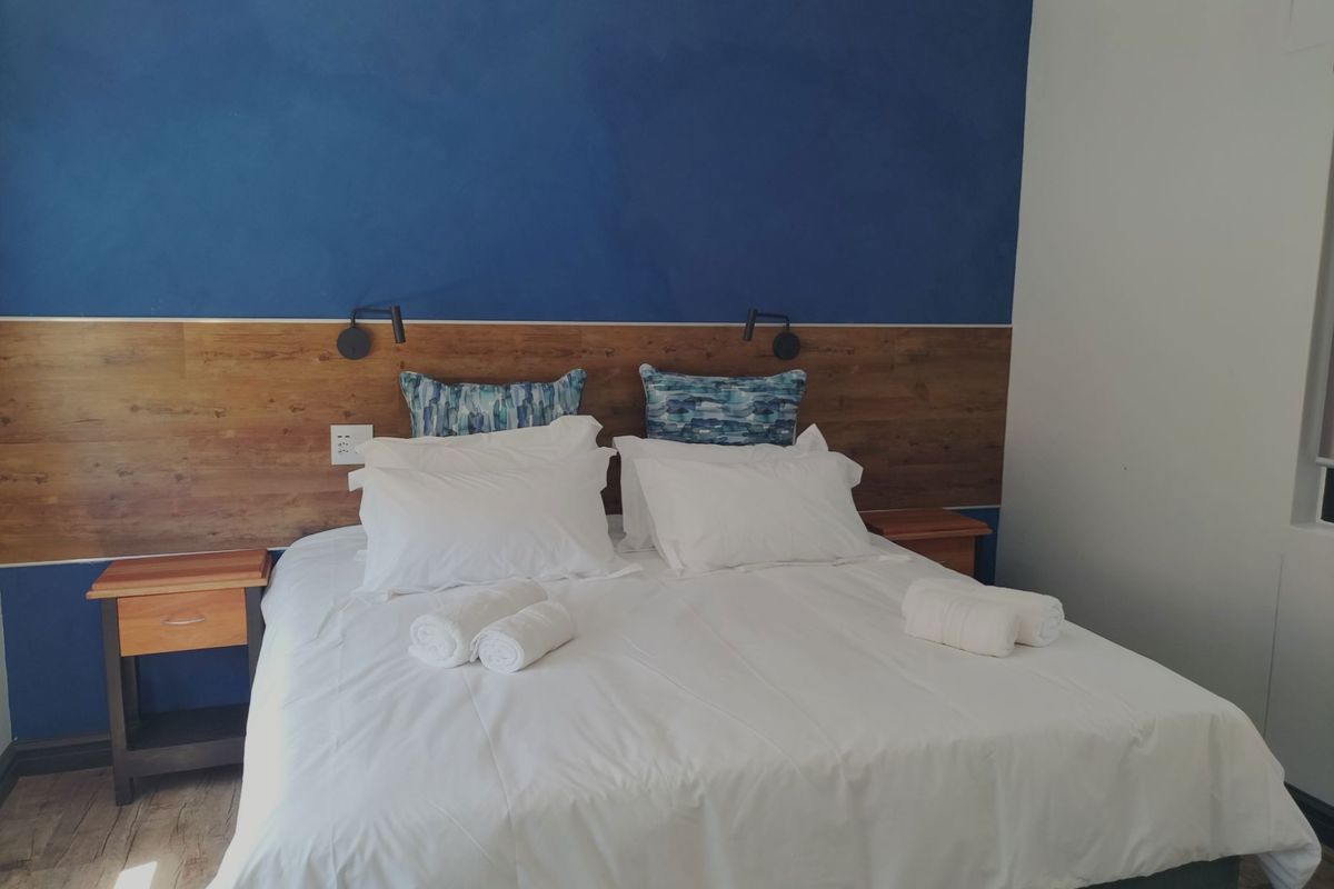 A well-maintained bedroom featuring a modern blue accent wall, wood-panelled headboard with integrated reading lights, and durable laminate flooring.