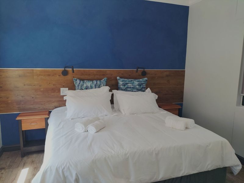 A well-maintained bedroom featuring a modern blue accent wall, wood-panelled headboard with integrated reading lights, and durable laminate flooring.
