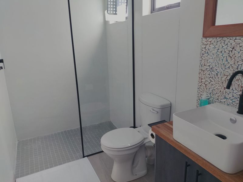 Modern bathroom featuring a walk-in shower with glass screen, vessel sink on a vanity cabinet, and decorative mosaic tile backsplash.