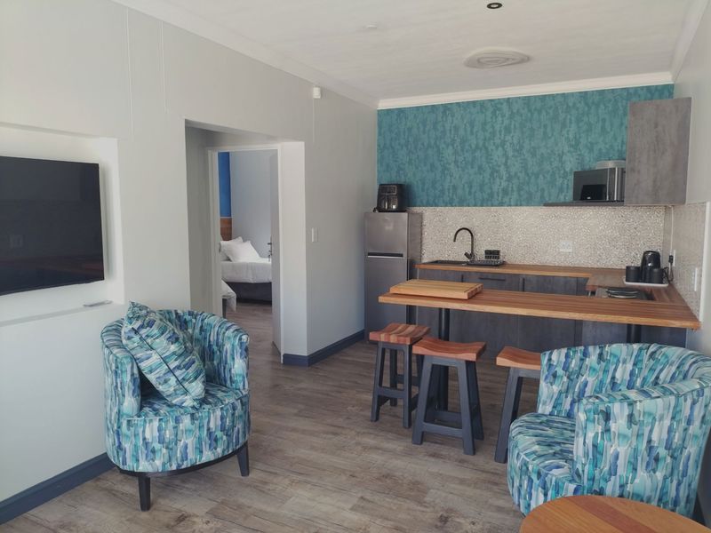Open-plan living area featuring a compact kitchenette with built-in cabinetry, breakfast bar, and direct access to an adjoining bedroom.