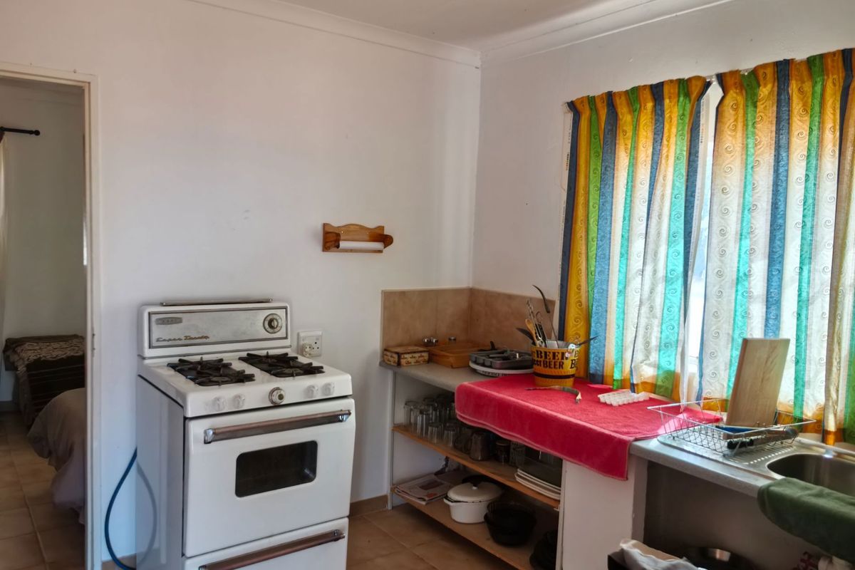 A functional kitchen area featuring a gas stove, open shelving, and a stainless steel sink with tiled splashback.