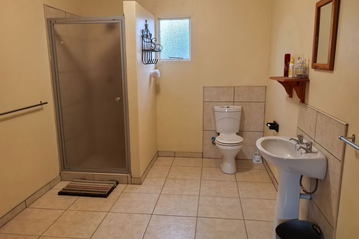 A functional bathroom featuring a shower enclosure, pedestal basin, and toilet with neutral tiled flooring and splashbacks.