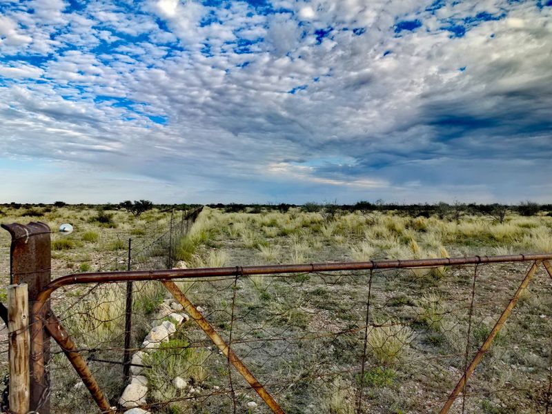 A view of the expansive farm landscape featuring a rustic metal gate, wire fencing, and a stone border under a dramatic cloudy sky.