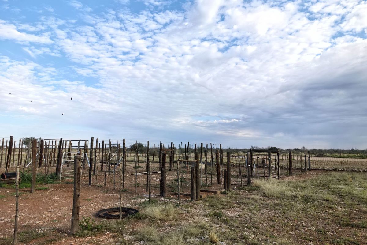 An expansive farm area featuring traditional wooden post and wire fencing with integrated metal gates, set against a rural landscape.