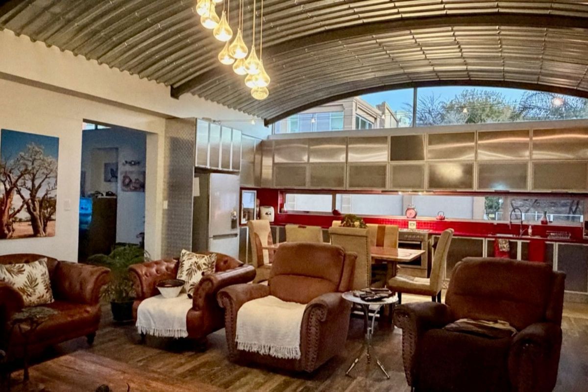 Spacious open-plan living and kitchen area featuring a unique corrugated metal barrel vault ceiling, modern stainless steel cabinetry, and warm laminate flooring.
