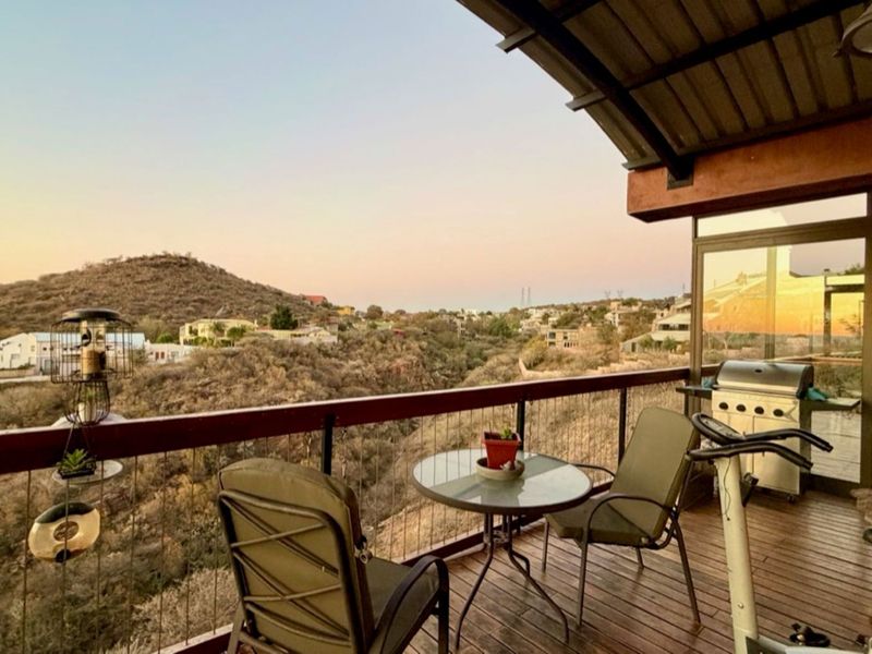 A covered balcony featuring timber decking and metal railings, offering expansive elevated views of the surrounding landscape and neighborhood.