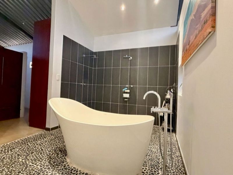 Modern bathroom featuring a contemporary freestanding bathtub, floor-mounted faucet, and stylish pebble flooring with dark tiled shower wall accents.