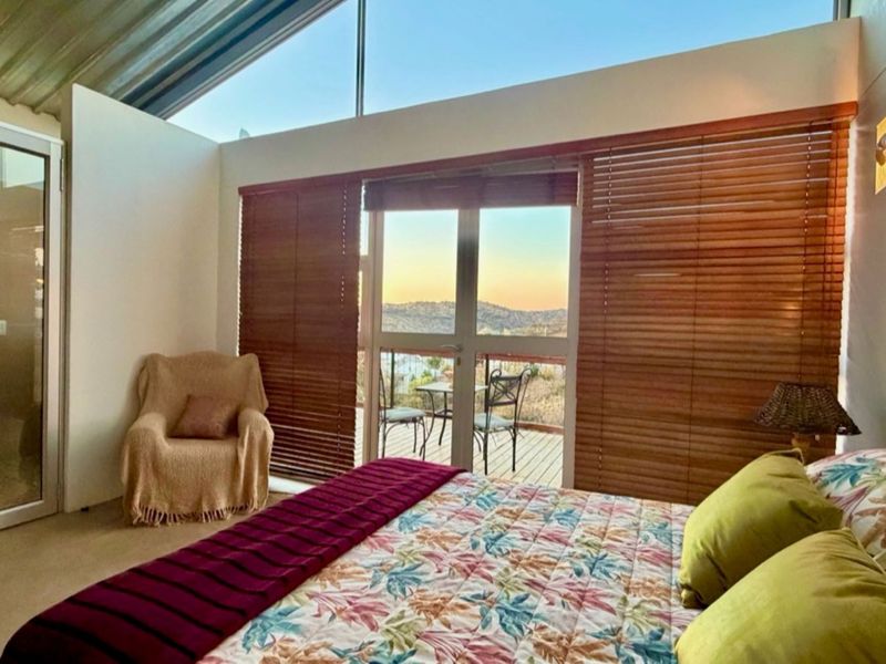 A bright bedroom featuring a sloped ceiling, clerestory windows, and a glass sliding door opening onto a private balcony with scenic views.