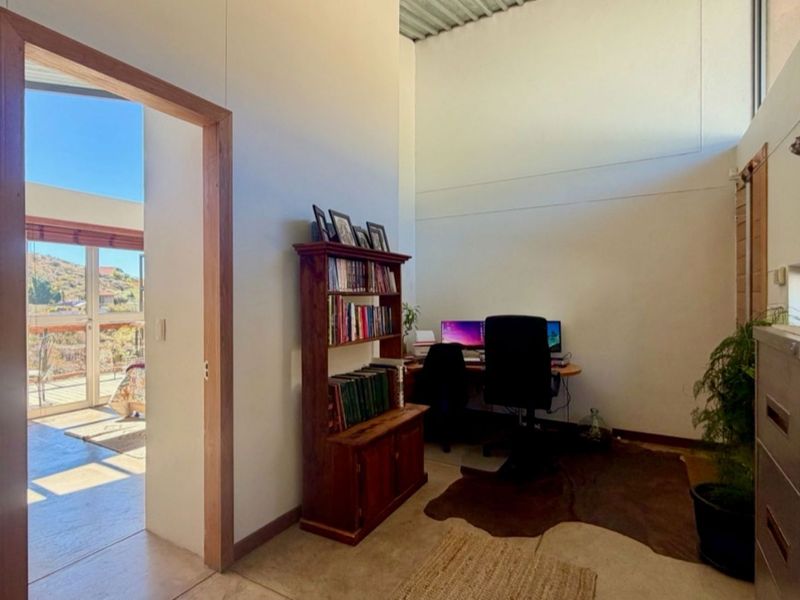 A bright home office featuring high ceilings with exposed corrugated metal, tiled flooring, and a doorway leading to an outdoor patio area.