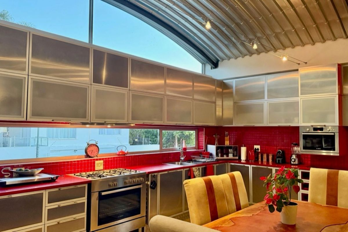 Modern kitchen featuring stainless steel cabinetry, vibrant red tiled backsplash, integrated gas cooktop, built-in oven, and a unique curved ceiling with clerestory windows.