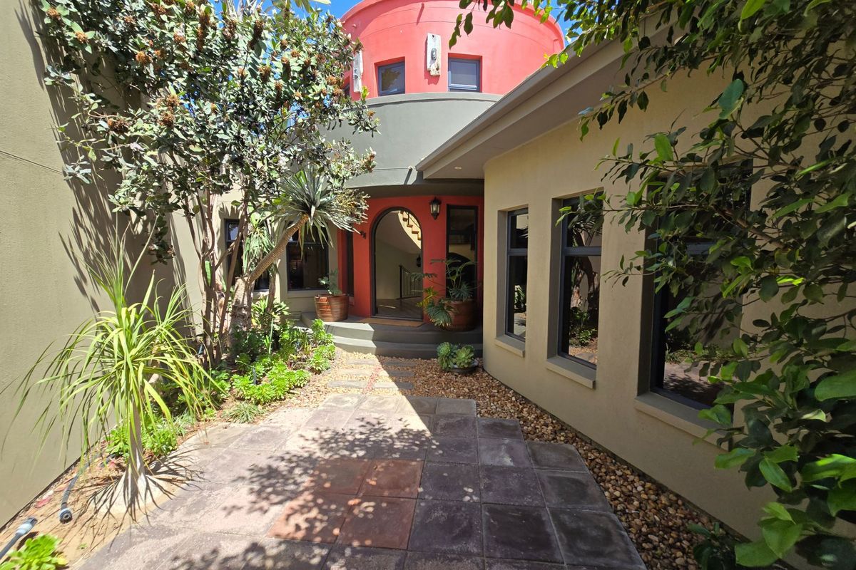 A well-maintained rear courtyard featuring a unique circular architectural design, paved flooring, and established garden beds leading to an arched entrance.