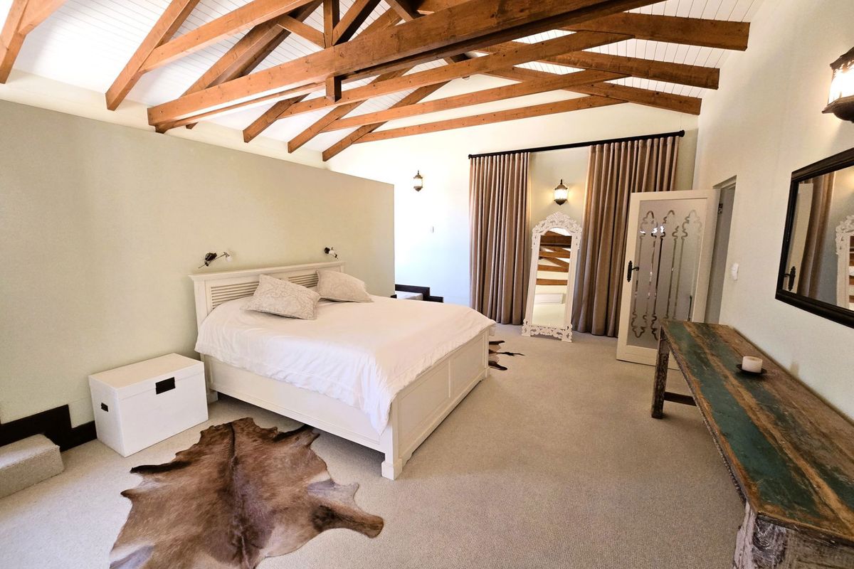Spacious bedroom featuring high vaulted ceilings with exposed timber trusses, neutral wall finishes, fitted carpeting, and elegant decorative door detailing.