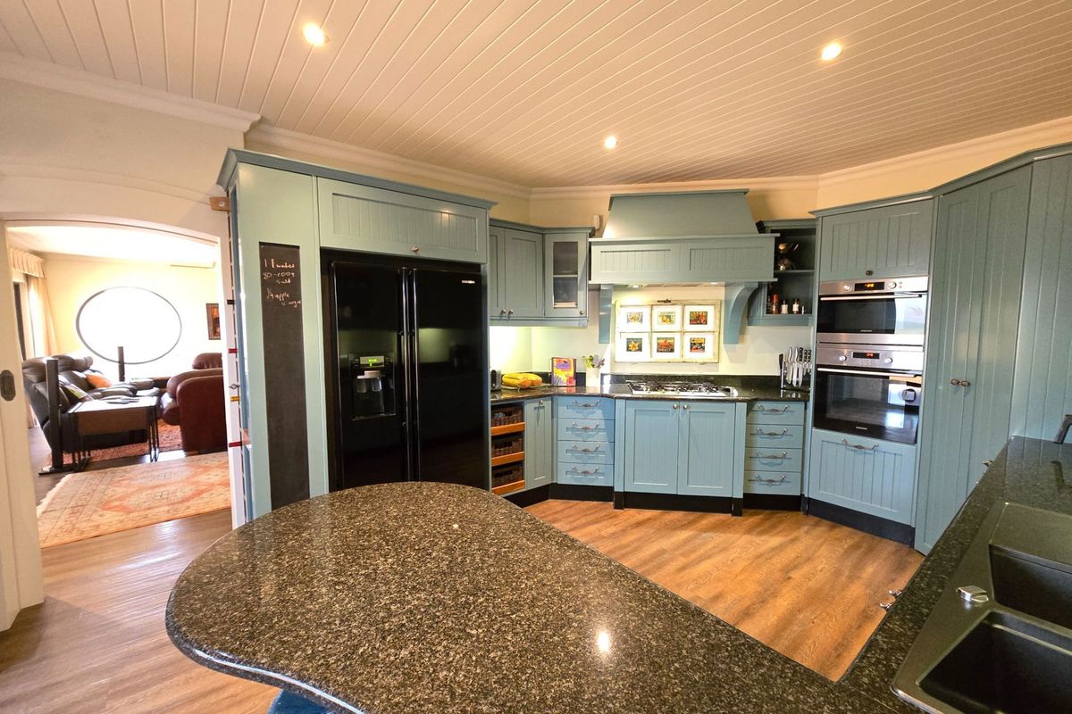 A well-appointed kitchen featuring custom blue cabinetry, granite countertops, integrated appliances, and a central island, with a view into the adjacent living area.