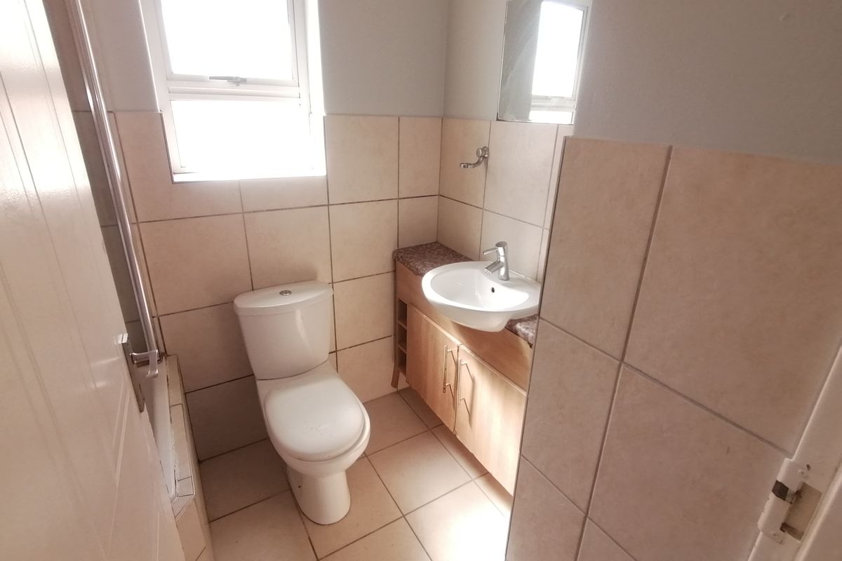 A functional bathroom featuring a vanity cabinet with a basin, a toilet, and neutral wall and floor tiling.