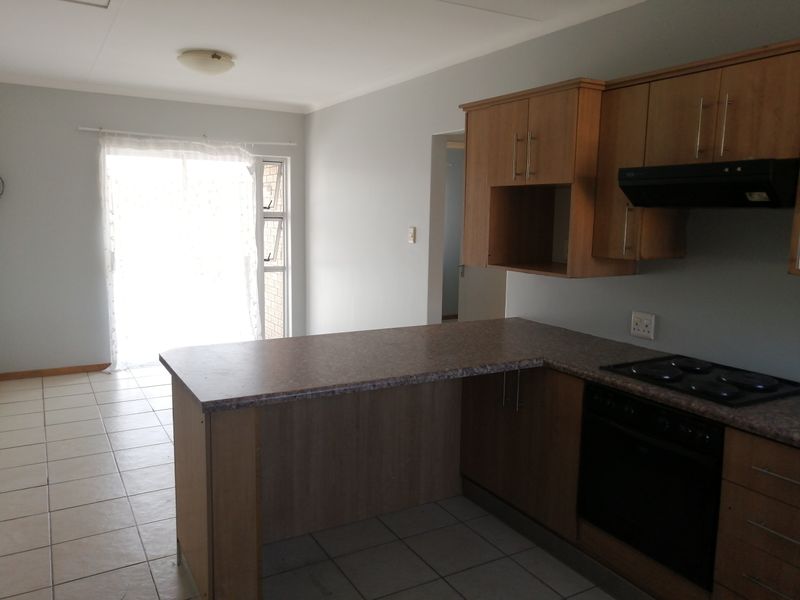 Open-plan kitchen and living area featuring wood-finish cabinetry, built-in appliances, tiled flooring, and a sliding door providing access to the exterior.