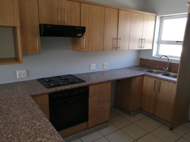 A functional kitchen featuring light wood-finish cabinetry, laminate countertops, a built-in oven with hob, and a double bowl sink with tiled splashback.
