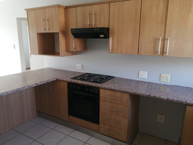 A functional kitchen featuring laminate cabinetry, built-in oven, electric hob, extractor fan, and tiled flooring, offering a clean and practical workspace.