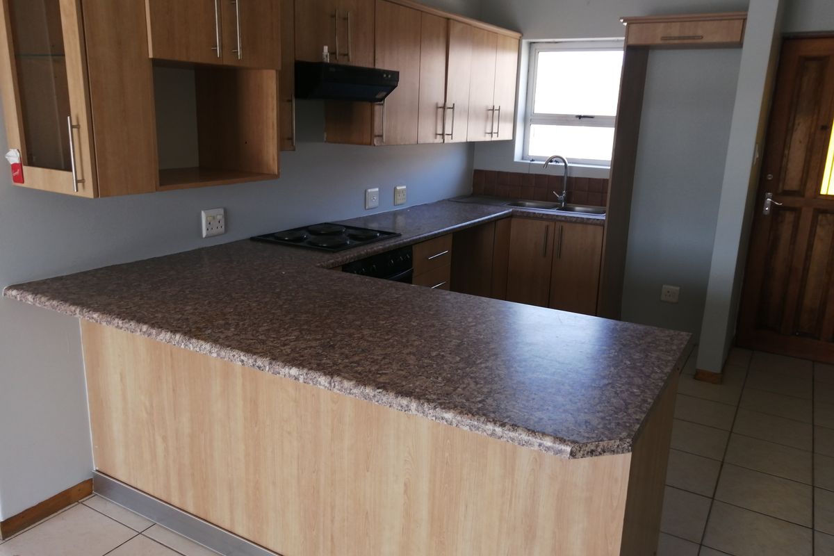 A functional kitchen featuring laminate cabinetry, stone-look laminate countertops, a built-in electric hob with extractor, and tiled flooring.