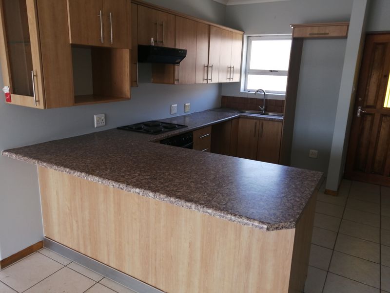 A functional kitchen featuring laminate cabinetry, stone-look laminate countertops, a built-in electric hob with extractor, and tiled flooring.