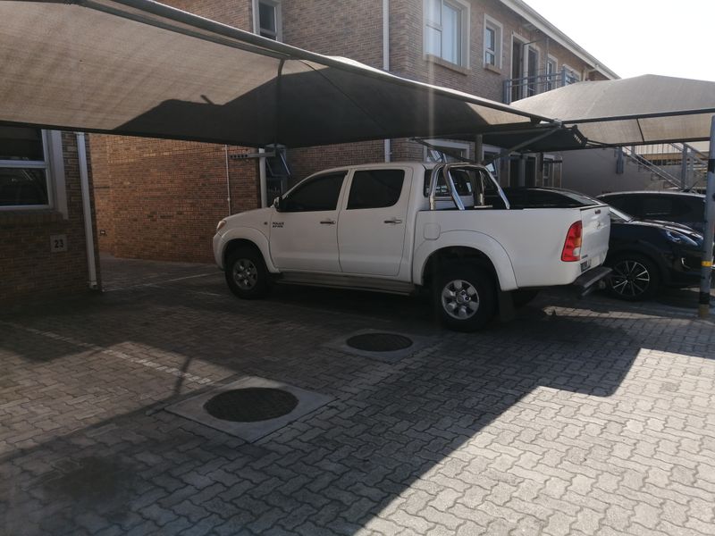 Exterior view of the property showing a paved parking area with shade cloth carports and brick building facade.