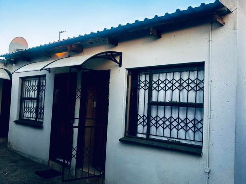 Front exterior view of the property featuring security gates, burglar bars on windows, and a covered entrance area with concrete paving.
