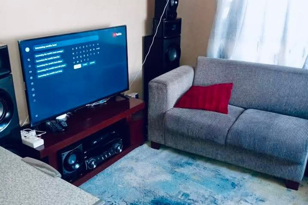 A living room area featuring a television setup and seating space, with natural light entering through the window.