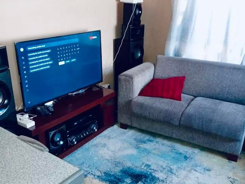A living room area featuring a television setup and seating space, with natural light entering through the window.