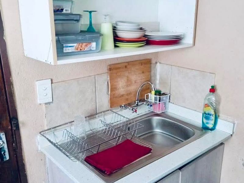 A compact scullery or wash-up area featuring a stainless steel sink, tiled splashback, and basic wall-mounted and base cabinetry.