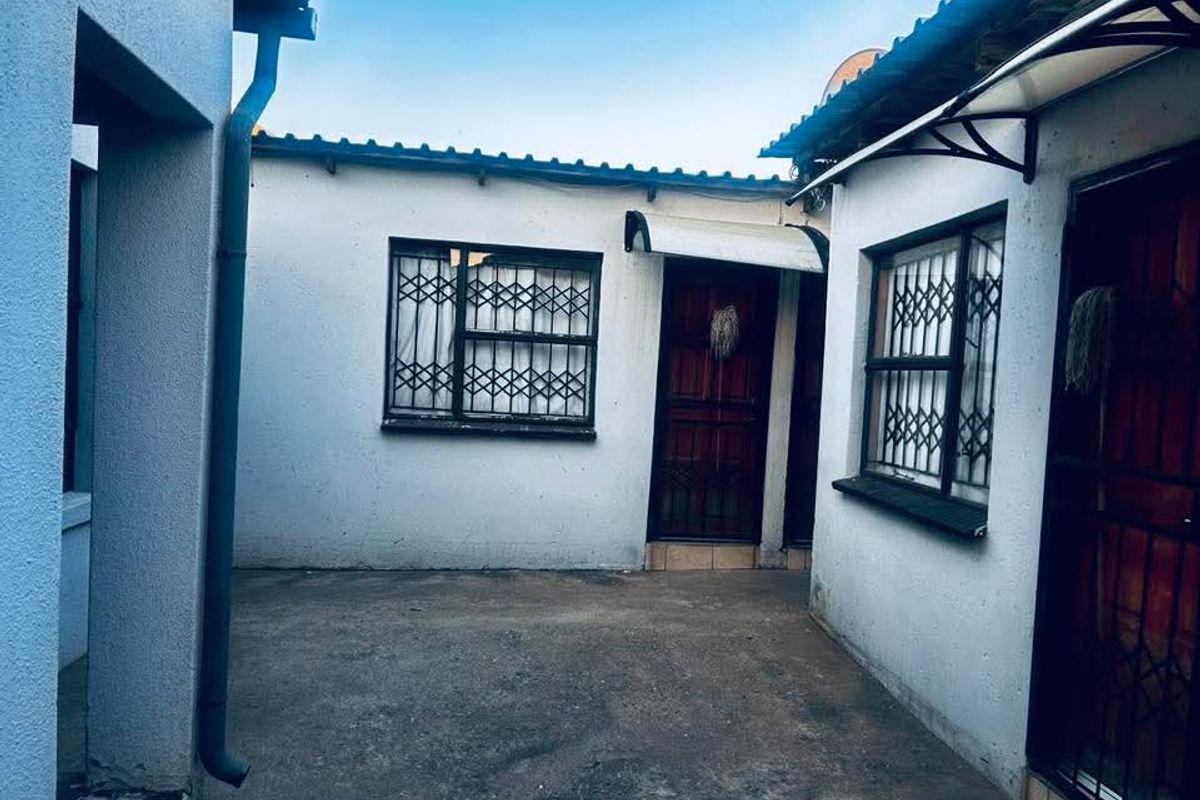 A paved rear courtyard area featuring security gates and bars on windows, providing a functional outdoor space with potential for landscaping improvements.