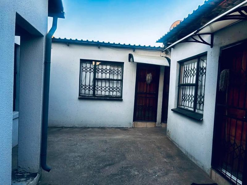 A paved rear courtyard area featuring security gates and bars on windows, providing a functional outdoor space with potential for landscaping improvements.