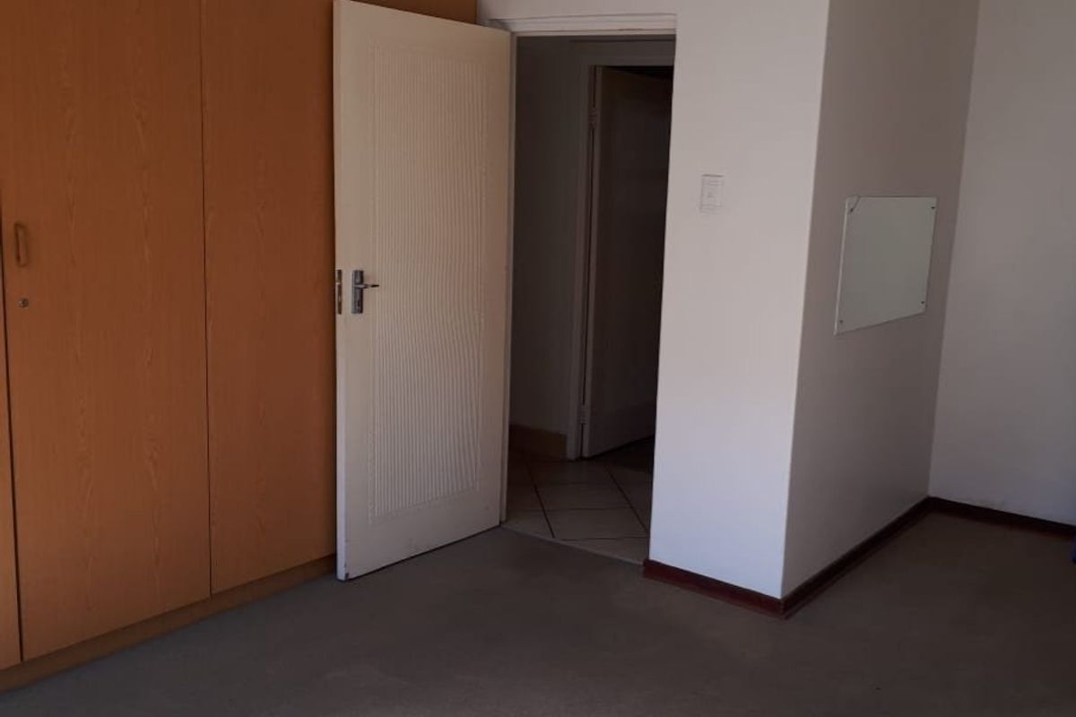 A bedroom featuring built-in wooden cupboards and carpeted flooring, with an adjacent doorway leading to a tiled hallway.