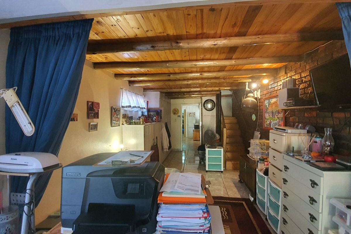 A living area featuring exposed timber beam ceilings, a rustic brick wall, and a staircase leading to the upper level.