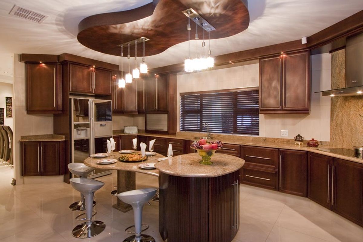Spacious kitchen featuring dark wood cabinetry, granite countertops, a central island with integrated seating, and a decorative recessed ceiling feature with pendant lighting.
