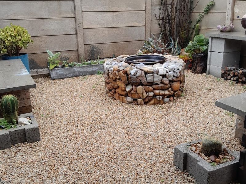 A low-maintenance rear courtyard featuring a central gabion fire pit, gravel ground cover, and precast concrete boundary walls.