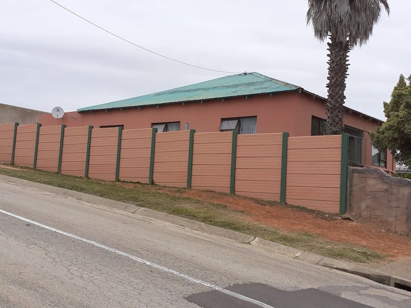 Street view of the property featuring a prominent precast concrete boundary wall and a corrugated metal roof.
